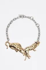 Collar de cadena plateada con dos dijes centrales en forma de panteras doradas enfrentadas. Las panteras presentan detalles de manchas en esmalte negro e incrustaciones de vidrio. Cuenta con un cierre de barra tipo T ajustable.