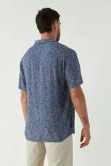 Camisa de manga corta con cuello cubano, confeccionada en viscosa con estampado de hojas en tonos azules. Presenta cierre frontal abotonado y corte slim.