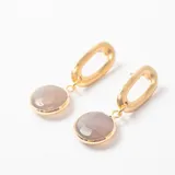 Caravanas colgantes compuestas por un eslabón ovalado de metal dorado y un dije circular con piedra facetada en tono gris.