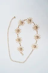 Cinturón de cadena metálica color dorado, compuesto por una serie de dijes en forma de sol con rostros grabados, unidos por eslabones. Incluye cadena de ajuste con cierre de mosquetón.