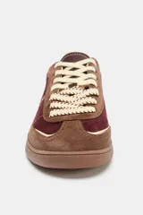 Zapatillas deportivas de caña baja con combinación de colores y materiales. El cuerpo principal es de color bordó, con refuerzos en gamuza marrón y detalles en color crema. La suela es de goma marrón. El cierre es mediante cordones gruesos color crema.