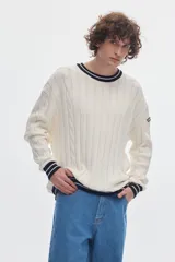 Buzo de punto blanco crudo con tejido de ochos y diseño regular. Cuenta con cuello redondo, puños y ruedo acanalados en color negro con líneas blancas en contraste.