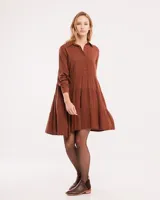 Vestido corto marrón con cuello camisero, abotonado en el frente, mangas largas con elástico en los puños y falda escalonada con volados.