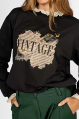 Sweater negro de algodón con cuello y puños de encaje, y estampado frontal con la palabra "Vintage" sobre un fondo de texto antiguo.