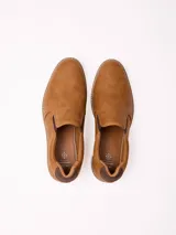 Zapatilla tipo slip-on color marrón, con diseño minimalista, elásticos laterales para mayor comodidad y suela blanca con detalle de costura visible.