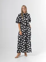 Conjunto de dos piezas con estampa polka dots en negro y blanco, compuesto por un pantalón tipo culotte de tiro alto con bolsillos y una blusa estilo camisa con mangas globo y cierre frontal de botones.