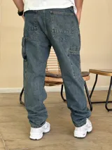 Pantalón tipo carpenter de denim azul con corte holgado, bolsillos laterales utilitarios y cierre frontal con botón.