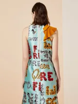 Vestido midi celeste con estampado de flores y texto, con volado amarillo en diagonal y lazo en el cuello.