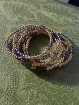 Pulsera elástica compuesta por una alternancia de cuentas metálicas doradas y cristales facetados de color violeta.