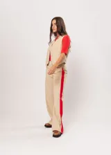 Pantalón beige de tiro alto con bolsillos delanteros y traseros, cierre frontal con cremallera y botón, y detalle de pespuntes rojos en los laterales.