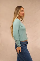 Saco de punto celeste de manga larga, con cuello redondo y cierre frontal de botones marrones. Presenta detalles de costura en contraste en el cuello, puños y ruedo.