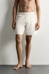 Short de baño largo en color beige, confeccionado en tejido técnico con tacto aterciopelado. Cuenta con cintura elástica ajustable con cordón, bolsillos laterales y detalle de bolsillo trasero, además de forro interior.