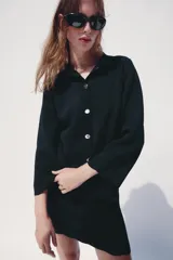 Chaqueta de punto color azul marino, con cuello solapa, manga larga y cierre frontal con botones metálicos. Presenta terminaciones en ondas en el bajo y los puños.