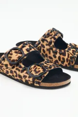 Sandalia tipo birkenstock de pelo con estampado animal print (leopardo), con dos tiras ajustables y tachas metálicas negras. La plantilla es de corcho y la suela de goma eva.