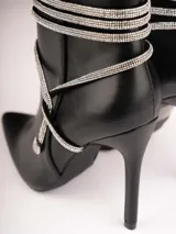 Botines plateados con terminación en punta y taco aguja. Decorados con tiras de strass que se enrollan alrededor del tobillo y se atan en el empeine.