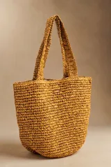 Bolso tipo tote color camel, confeccionado en material trenzado con textura rústica, doble asa de hombro y pequeño aplique metálico con el logo de la marca.
