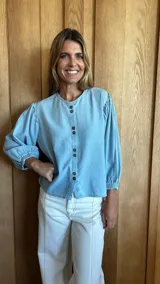 Camisa de jean celeste con cuello redondo, mangas abullonadas y puños elásticos. Cierre frontal con botones.