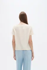 Blusa de viscosa color natural, con cuello a la base, manga corta y detalle de plisado cruzado en el frente. Presenta un corte holgado.