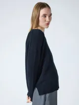Sweater de cachemira color negro para mujer, con cuello redondo y corte oversized. Presenta costuras externas decorativas, hombros caídos y un diseño ligeramente más largo en la parte trasera con aberturas laterales. Los puños y el bajo cuentan con acabado acanalado.