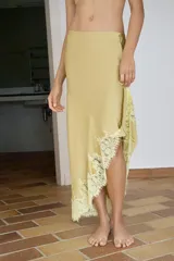 Falda midi de tiro medio confeccionada en tejido satinado color beige. Presenta un diseño asimétrico con costuras marcadas y aplicación de encaje a tono en el bajo. Cuenta con cierre lateral oculto.