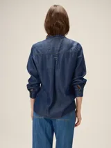 Camisa de denim liviano color azul, con cuello mao y detalles de volados fruncidos en el cuello y la botonera frontal. Presenta mangas largas con puños rectos y corte relajado.
