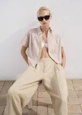 Pantalón Deia de corte recto y largo, color beige, con detalle de pinzas, trabillas y bolsillos laterales. Cuenta con cierre oculto de botón, gancho y cremallera, y forro interior.