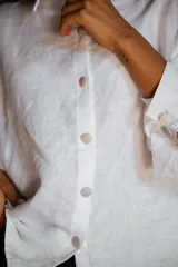 Camisa de lino de corte relajado y silueta holgada, con cuello clásico y cierre frontal de botones forrados en lino a rayas. Presenta mangas largas con puños amplios.