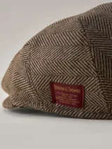 Boina estilo irlandés con diseño de espigado en tonos marrones y beige. Presenta una etiqueta decorativa lateral en color rojo.
