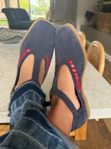 Ballerina tipo T-strap confeccionada en cuero gamuzado color azul marino, con detalle de costura artesanal en color rojo a lo largo de la abertura central y suela plana.