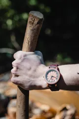 Reloj de pulsera con caja, esfera y malla de madera de sándalo rojo, con marcadores y manecillas negras. Presenta un diseño circular con corona lateral.