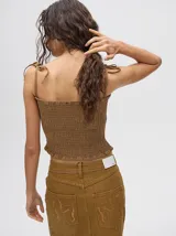 Top crop de tela denim con efecto fruncido, breteles finos ajustables con lazos y diseño entallado al cuerpo.