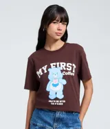 Remera de algodón color marrón con cuello redondo y manga corta. Presenta una estampa frontal de un osito de la serie Los Cariñositos sosteniendo una taza de café, acompañada por el texto 'My First Coffee' y 'Talk to me after ten o'clock'.