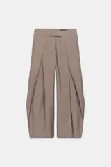 Pantalón de tiro medio color gris, con bolsillos delanteros, pliegues marcados y diseño abombado en las piernas. Cuenta con cierre frontal con cremallera y ganchos metálicos ocultos.