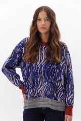 Buzo de punto con estampado abstracto en tonos azul, beige y marrón. Tiene cuello redondo, puños y ruedo acanalados en color ladrillo y gris.