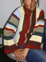Sweater tejido a mano con terminaciones en crochet, de silueta oversize y mangas acampanadas. Presenta un diseño de rayas verticales y horizontales en tonos tierra, crema, verde y azul claro.