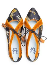 Zapato tipo blucher de raso negro con bordado de libélulas en color ocre. Presenta detalles en terciopelo ocre en los laterales y el talón, con un borde festoneado y costuras en zigzag. Se ajusta con cordones de algodón rematados con borlas de ante.