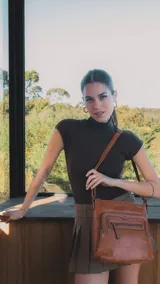 Bandolera de cuero sintético color marrón, con dos bolsillos frontales con cierre y detalles de tachas metálicas. Incluye un bolsillo trasero y tres bolsillos internos. Correa larga regulable.