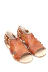 Sandalia baja de cuero en tono mostaza con detalles en cuero marrón, diseño de aberturas laterales y cierre con hebilla metálica ajustable en el tobillo.
