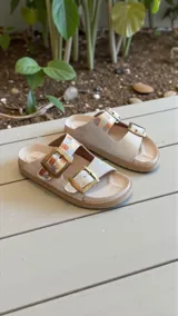Sandalias planas de cuero color blanco, con dos tiras anchas ajustables mediante hebillas metálicas doradas y detalles pintados a mano en tonos multicolores.