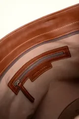Cartera tote de cuero suave color marrón, con diseño amplio y líneas simples, con tiras de hombro decoradas con nudos artesanales y pequeño logo grabado en el centro.