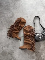 Botas altas de gamuza marrón con diseño slouchy, punta fina y flecos largos colgantes en los laterales.