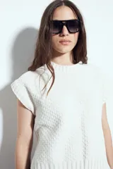 Chaleco tejido sin mangas de color negro, con cuello redondo y diseño de textura sutil. Presenta un corte recto con terminaciones acanaladas en el ruedo y hombros levemente estructurados.