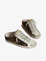 Zuecos Golden Goose modelo Super-Star Sabot, con diseño de zapatilla sin talón. Presentan exterior cubierto de glitter negro y dorado, estrella característica en el lateral, cordones y forro interior de shearling sintético.