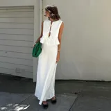 Conjunto de top y falda color crema, confeccionado en lino. El top es sin mangas, con detalle de lazos en el escote y volados en el ruedo. La falda es larga y de corte recto.