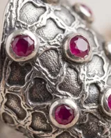 Anillo ancho de plata con diseño texturizado en relieve y pequeñas piedras circulares de rubí incrustadas.