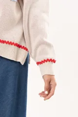 Sweater tejido color crudo con cuello redondo y mangas largas. Presenta dos peces rojos con detalles en azul bordados en el frente. Tiene ribete ondulado rojo en cuello, puños y ruedo.