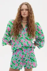 Camisa celeste con estampado floral en tonos rosados y verdes, de lino, con cuello camisero, mangas largas abullonadas y cierre frontal con botones.