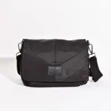 Bandolera negra de tela acolchada con diseño geométrico. Tiene correa de hombro ajustable y cierre con solapa.