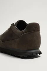 Zapatilla deportiva de hombre confeccionada en piel con acabado de serraje, diseño de paneles y suela dentada.