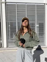 Buzo de tejido suave color verde oliva, con diseño holgado, cuello polo abierto y mangas largas con puños ajustados.